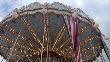Top part of carousel with horses. The roof of attraction spins, lights flash against sky. Horizontal 4k. video