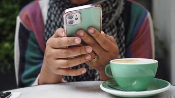 A person utilizing their smartphone while savoring a warm cup of coffee in a cozy cafe video