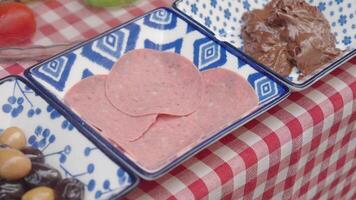 An inviting display of sliced deli meat and a chocolate spread on patterned plates. video