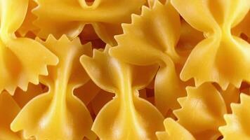 Uncooked Farfalle Pasta. A Culinary Canvas of Bow-Tie Macaroni, Creating a Lively and Textured Background for Gourmet Cooking - Top View, Rotating. Turning Dry Pasta. Raw Macaroni - Rotation video