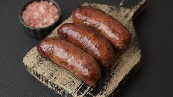 Juicy sausages with salt, spices and herbs grilled on a dark concrete background video