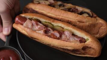 Hotdog with grilled sausage with bacon and mushrooms in a bun with salt, spices and herbs video