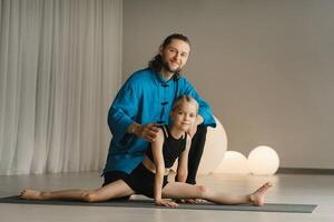 A yoga instructor in training helps a child to do exercises in the gym photo