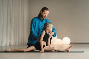 A yoga instructor in training helps a child to do exercises in the gym photo
