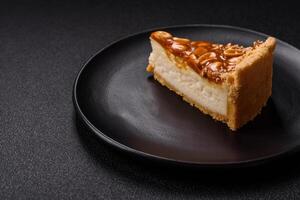 Delicious fresh cheesecake caramel peanut cake with cream and nuts on a ceramic plate on a dark concrete background photo
