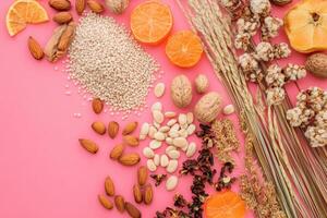 Healthy seeds, nuts, mandarin slices and dry flowers creating a vibrant pink background photo