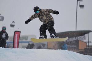 Snowboarder jumping high, performing tricks in snowy mountain terrain photo