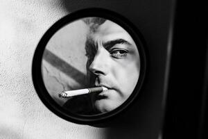 Man smoking cigarette reflected in round mirror black and white close up photo