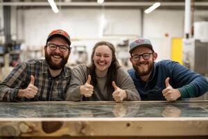 Smiling glass factory workers showing thumbs up behind finished work photo