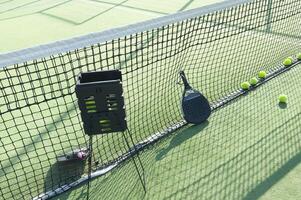 padel racket and yellow balls placed on court near net on sunny day photo