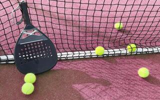 padel racket and yellow balls placed on court near net on sunny day photo