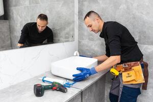 A man cleaning a bathroom sink with a scraper blade and micro fiber cloth to remove lime and stains photo