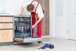 Concept maintenance service of home appliances. Worker cleans filter in the dishwasher. Male repairman checking food residue filters photo