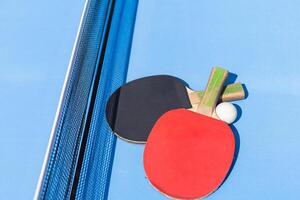Red and black Table Tennis Paddles and ball on the blue table tennis table with net. Ping Pong concept with copy space photo