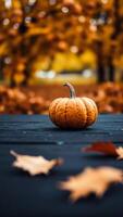 A Single Pumpkin on a Dark Wooden Table with Autumn Leaves in the Background photo