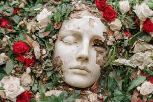 serene stone face surrounded by red roses and leaves photo
