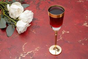 elegant glass of red wine with white roses on red marble background photo