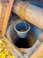 Old Wooden Water Well with Rusted Chain and Hanging Bucket in Autumn Setting. High quality photo