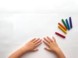 Childs hands preparing to draw with colorful crayons on white paper photo