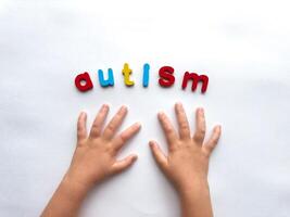 Childs hands and colorful letters spelling autism on white background photo
