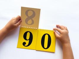 Childs hands flip through yellow pages with numbers. Displaying number 90 on white background photo