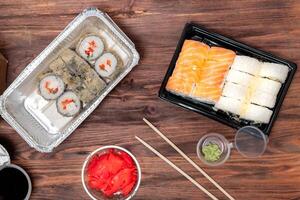 ordered food from an Asian cafe, fried rolls and tuna rolls, with ginger, soy sauce and wasabi in plastic packaging, on a wooden background photo