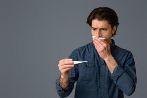 Sick Coughing Man Holding Thermometer, Checking His High Temperature, Standing Over Light Background In Studio, Copy Space photo