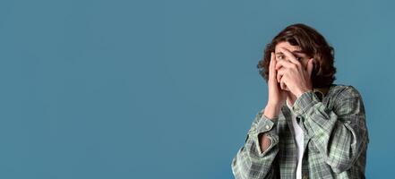 Anxiety and stress concept. Curly guy closing his face in fear on color background photo