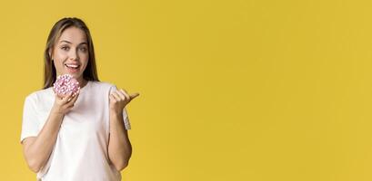 Tasty Sweets. Positive Millennial Lady Holding Donut And Pointing Aside At Copy Space On Yellow Background With Her Thumb Up, Panorama photo