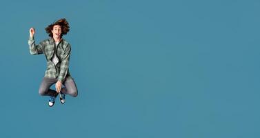 Happiness and freedom concept. Cheerful young guy in casual clothes jumping on turquoise background photo