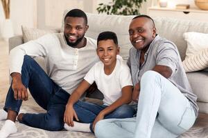 Cheerful African American Family Sitting On Floor At Home Posing To Camera. Father, Son And Grandfather Enjoying Spending Weekend Together photo
