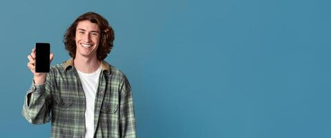 Smiling Caucasian guy holding smartphone with empty screen on turquoise background, space for your design photo