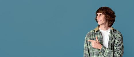Cool guy with curly hair pointing aside on color background, space for design photo
