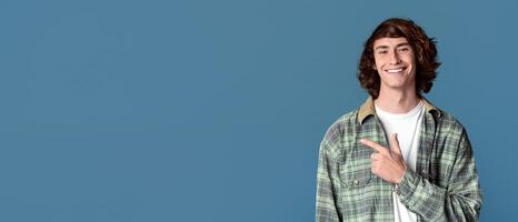 Confident teenager smiling and pointing aside on turquoise background, copy space photo