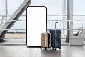 Two suitcases are positioned beside a large blank advertising display in a spacious airport terminal, with a view of planes and the runway in the background during the day. photo