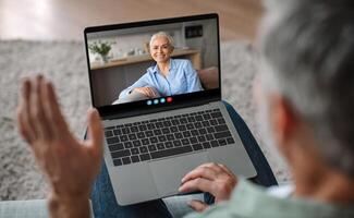 An elderly woman shares a warm smile while engaging in a call. Her cozy home setting and joyful demeanor create a heartwarming connection with her loved one. photo
