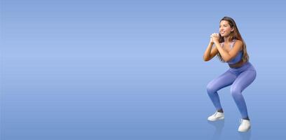 A woman is engaged in a squat exercise, showcasing her fitness routine. She wears a matching blue workout outfit and focuses on maintaining proper form while exercising. photo