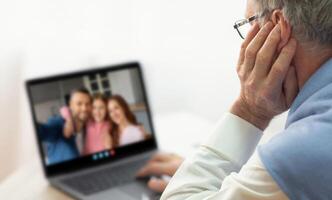 An elderly man is participating in a call with his family members, who appear joyful on the screen. He sits comfortably at home, enjoying the interaction. photo