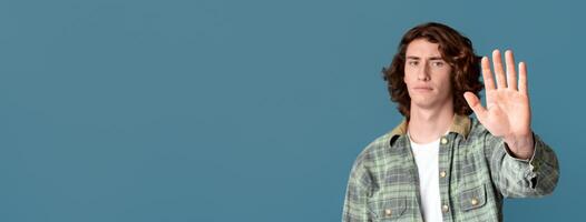 Expressing rejection. Serious young guy showing STOP gesture on color background photo