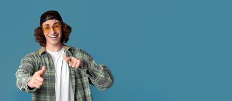 Portrait of cool young guy in sunglasses pointing at you on turquoise background photo