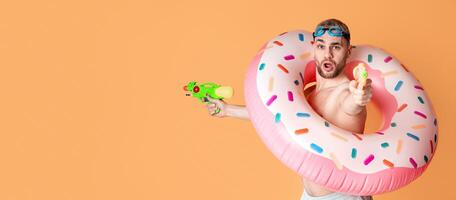 Expressive guy in inflatable ring shoots water guns with open mouth photo