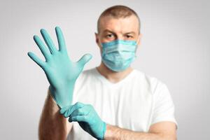 Virus Protection. Man In Medical Mask Putting On Rubber Gloves Standing Over Gray Background. Shallow Depth, Selective Focus photo