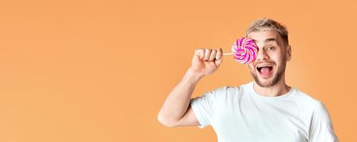 Happy millennial man with open mouth closes the eye with rainbow lollipop photo