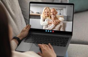 A person sits on a couch using a laptop to call a smiling couple who appear happy and engaged. The setting shows a cozy home environment filled with a warm atmosphere. photo