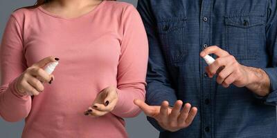 Precautions During Coronavirus Outbreak. Young couple applying disinfectant spray on hands to prevent spread of bacteria, light studio background photo