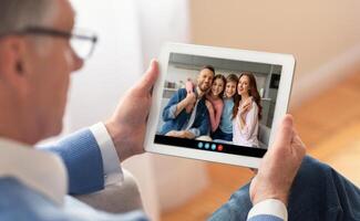 A man enjoys a call with his family, smiling as they connect on a tablet. The warm setting creates a cozy atmosphere filled with love and togetherness. photo
