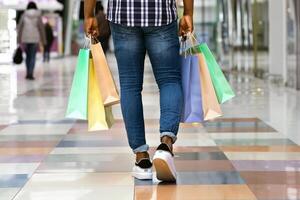 Sale And Consumerism Concept. Unrecognizable Black Man Walking In Shopping Mall With Purchases, Rear View Of African American Guy Carrying Lots Of Colorful Shopper Bags In Department Store, Copy Space photo