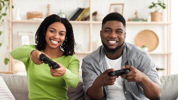 Couple Activities At Home. Cheerful black guy and lady playing games together, holding joysticks and competing with each other photo