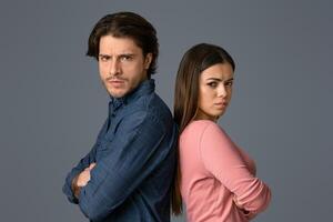 Relationship Crisis. Offended young couple standing back to back with folded arms and looking at camera, light studio background with copy space photo