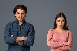 Millennial couple suffering from relationship problems, standing together offended after quarrel over light background in studio, free space photo